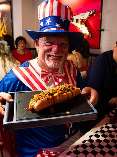 Su hot dog con crispy de cebolla, servido por el camarero vestido de Tío Sam